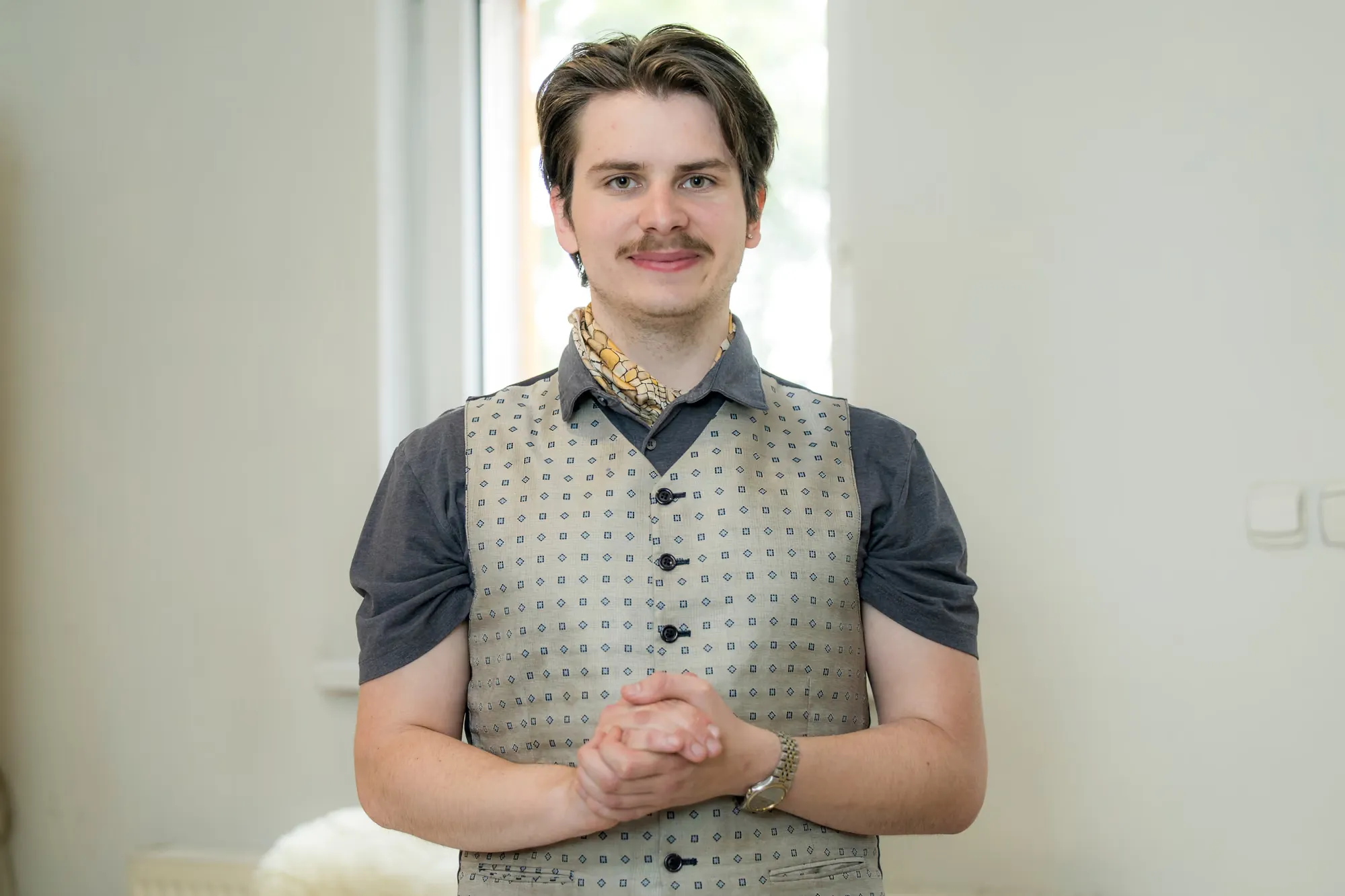 Aleksander w kamizelce we wzór i apaszce, uśmiechnięty, w jasnym wnętrzu