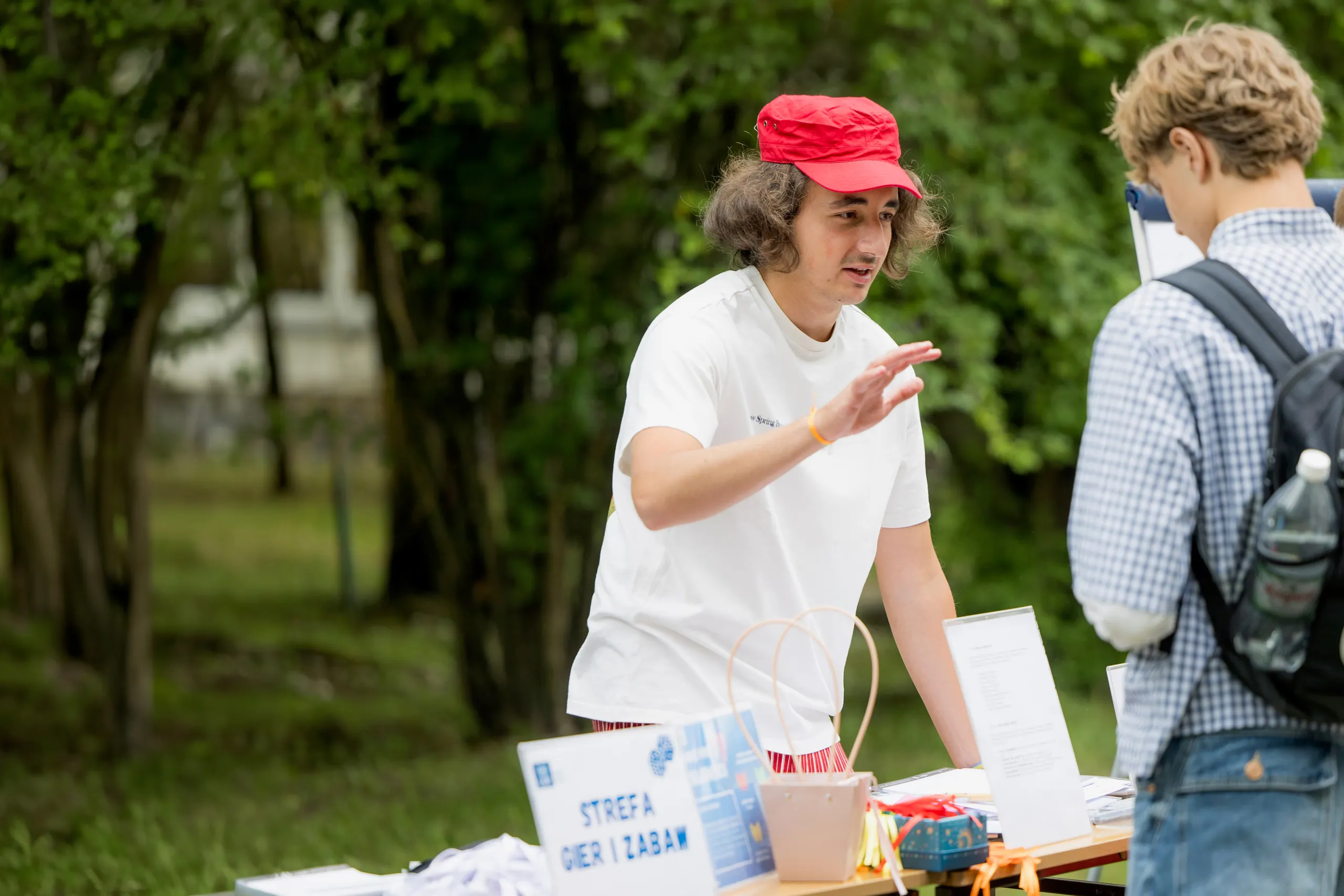 Kacper rozmawia z drugą osobą na zewnątrz, w czerwonej czapce