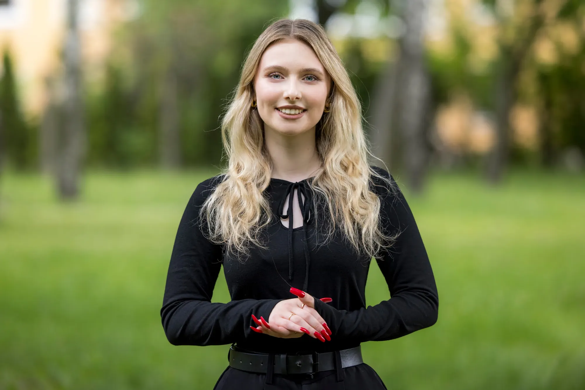 Małgorzata w czarnej bluzce, uśmiechnięta, na tle trawnika i drzew