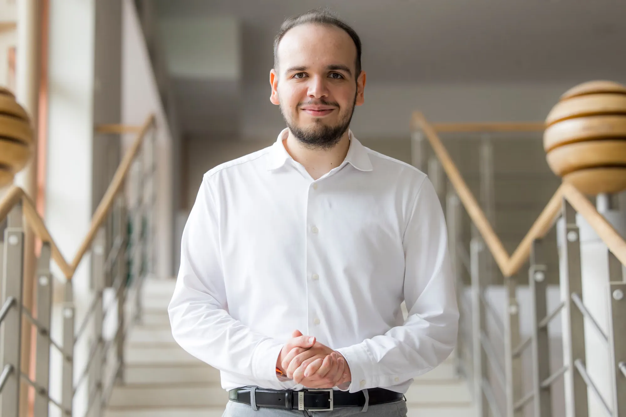 Piotr w białej koszuli, uśmiechnięty, na klatce schodowej budynku uczelni
