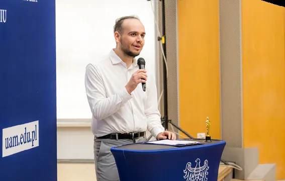 Piotr przemawia przy mównicy z mikrofonem podczas konferencji