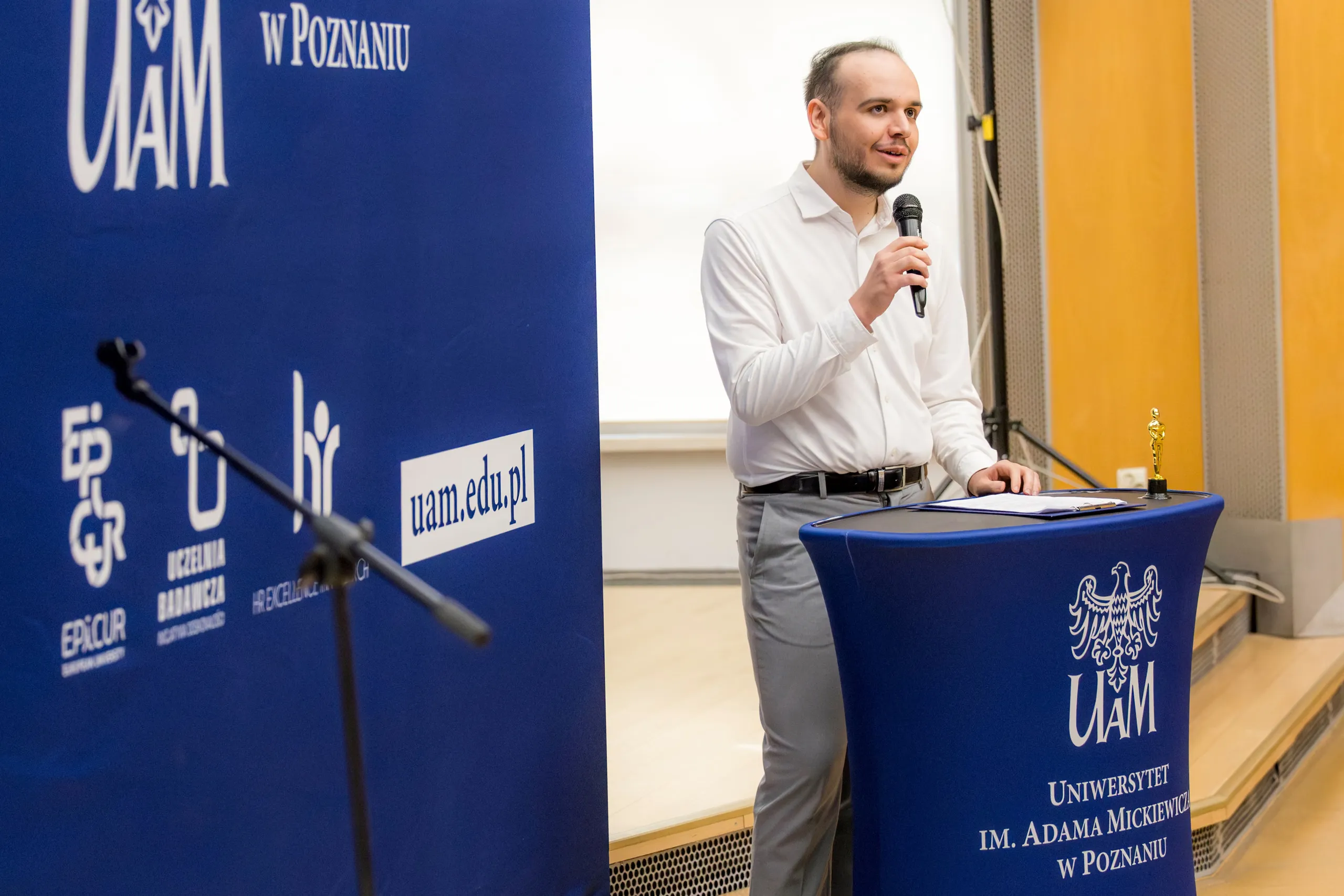 Piotr przemawia przy mównicy z mikrofonem podczas konferencji